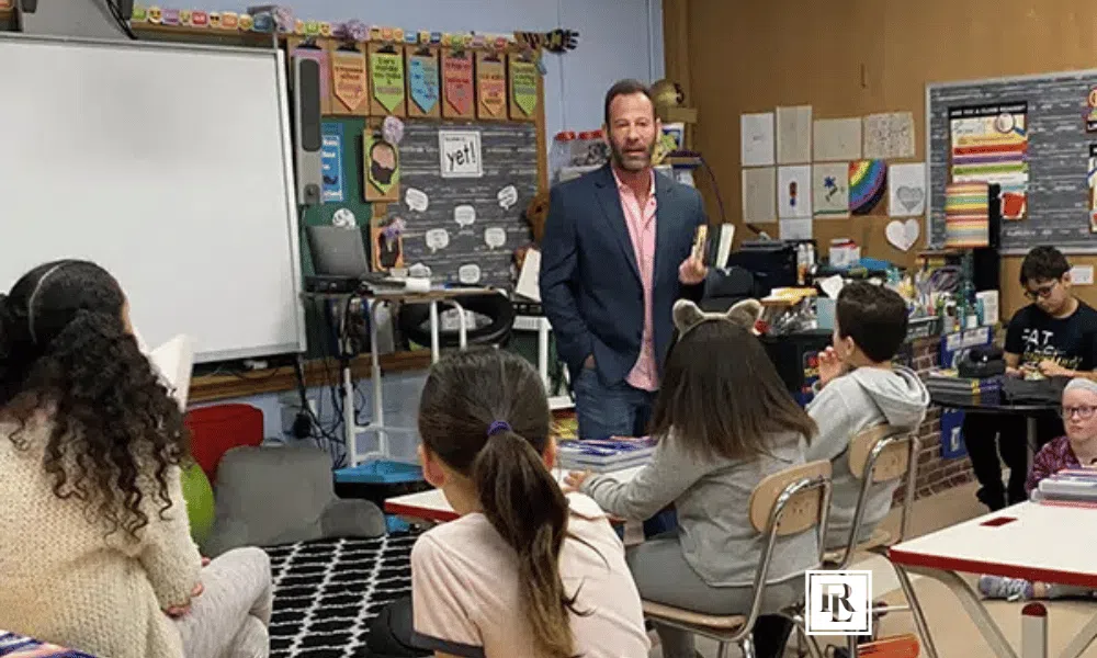 Rob Levine speaking in front of children in a classroom for reading week