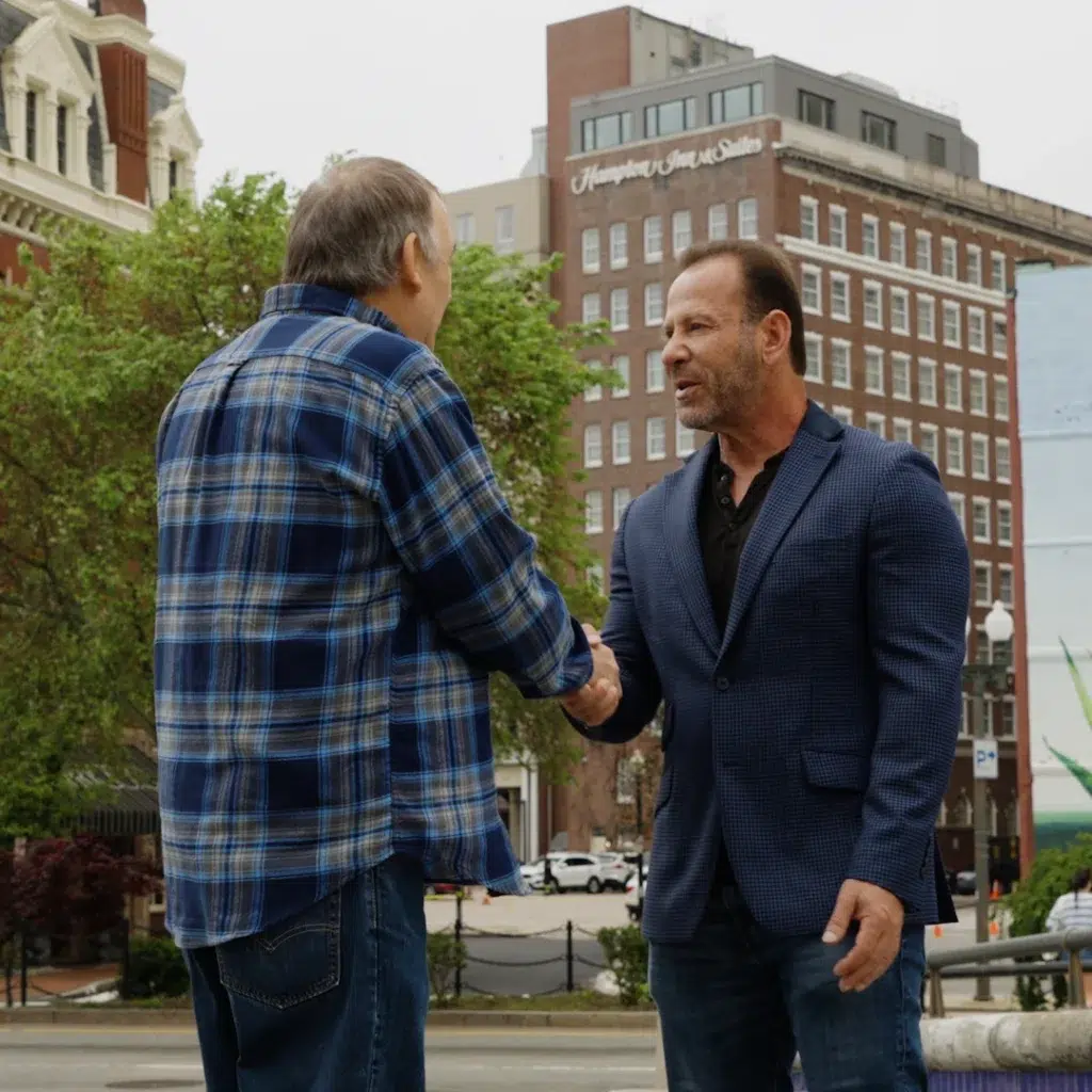 Rob Levine shaking hands with a happy client outside with multi story buildings in the background